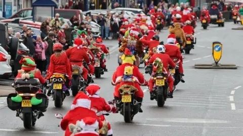 Joulupukuihin pukeutuneita motoristeja ajamassa kaupunkikadulla letkassa